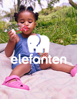 Happy girl blowing soap bubbles sitting on a blanket in a garden and wearing elefanten shoes